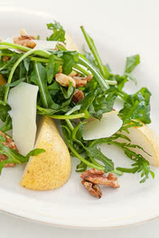 The image presents a salad featuring fresh arugula, thin pear slices, toasted walnuts, and hand-cut pieces of our Allgäu organic cheese, showcasing the region’s traditional craftsmanship and commitment to sustainable dairy farming.