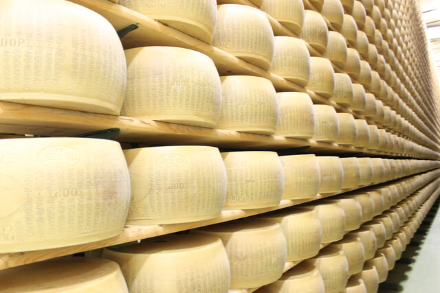 The image displays a careful stack of Parmigiano-Reggiano wheels, each aged under strict organic guidelines to deliver the authentic, complex flavor our customers expect.