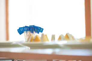 The image displays several small blue flags set into portions of our artisanal Allgäu cheese, highlighting the region’s time-honored dairy craftsmanship and the natural care that goes into every wheel.