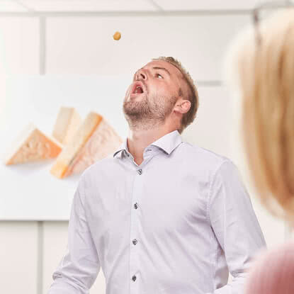 The image shows a man reaching for a small snack, while another person is in the background.