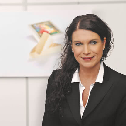 The image features a woman in professional attire, smiling and standing before a wall with a backdrop.