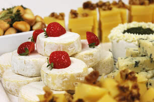 The image presents an assortment of our artisanal Allgäu cheeses, each garnished with fresh organic strawberries and accompanied by a selection of complementary snacks.