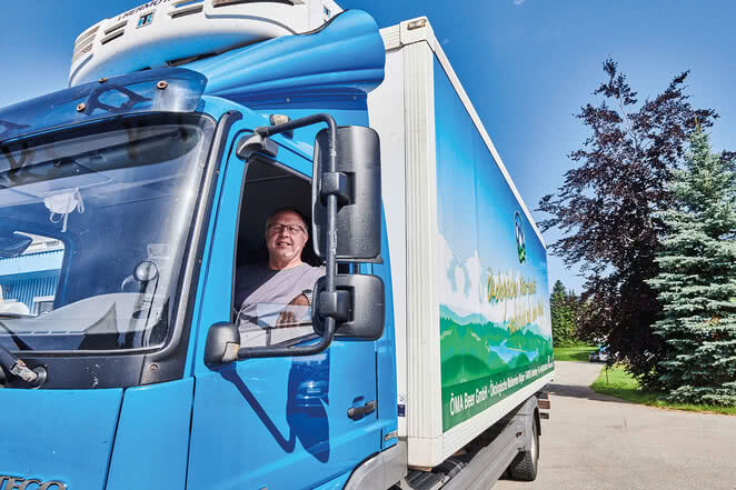 The image features a smiling man in the cab of a blue truck.