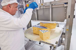 The image shows one of our cheesemakers in protective clothing, skillfully operating a machine to craft organic cheese.