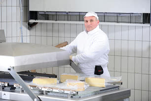 The image shows one of our master cheesemakers in protective clothing, standing by a pasteurization tank in our Allgäu creamery and shaping blocks of organic cheese.