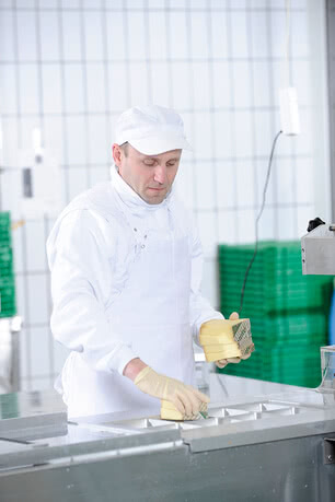 The image depicts a team member in our Allgäu creamery, wearing protective gloves and carefully crafting organic butter by hand.