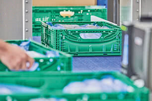 The image displays green plastic crates, some partially filled with blue and white materials, while a hand touches one of the crates.