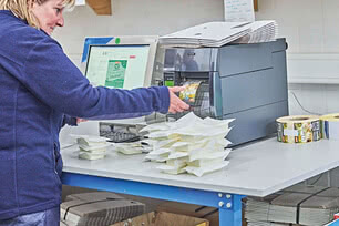The image shows one of our cheesemakers at work, carefully removing labels from a printer while additional packaging materials rest on the table.