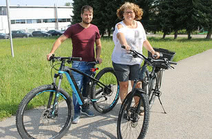 The image depicts a man and a woman standing beside their bicycles.