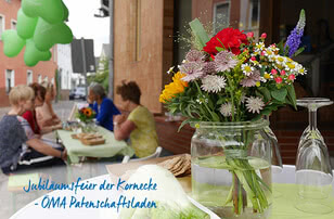 The photograph depicts a celebratory gathering to mark the anniversary of the ‘Kornecke’ department of the ÖMA charity shop, featuring floral arrangements and guests seated at tables.