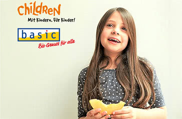 The image features a smiling girl holding a piece of fruit, alongside text that highlights our Allgäu-inspired children’s project and commitment to certified organic food.