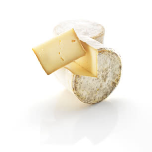 The image presents a wheel of our organic Allgäuer Bergkäse with a piece expertly cut away, revealing its rich, creamy interior.