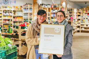 The photo shows two women proudly holding an award for the best organic shop of 2022, ‘Val Verde Naturkost’, in a grocery shop.