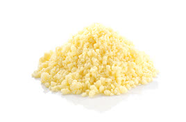 The image displays a heap of pale-yellow, grainy beeswax, a natural by-product of our Allgäu apiary.