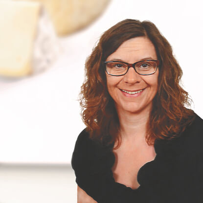 The image features a woman with curly hair and glasses, smiling.